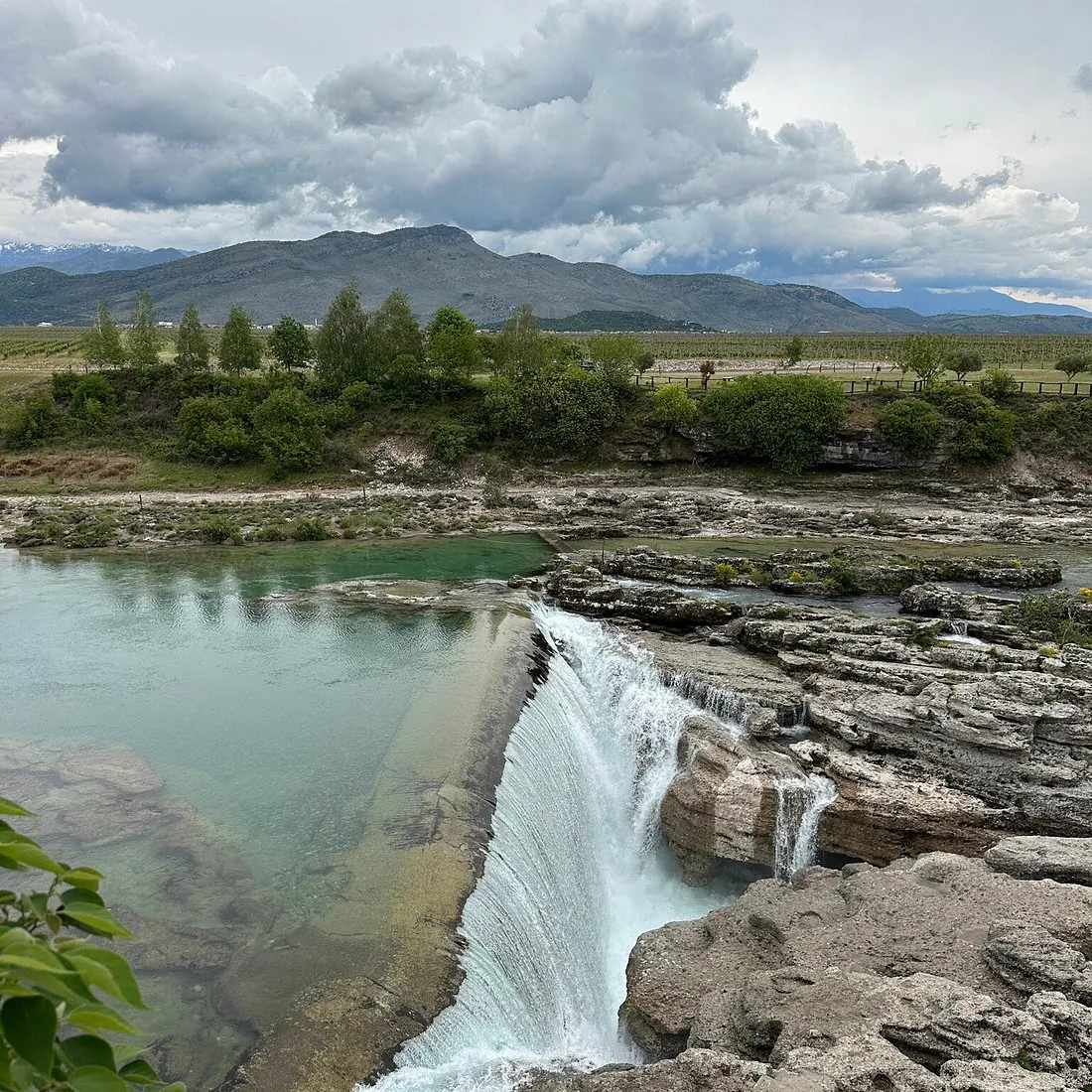Turquoise river and waterfall below cloud-covered mountains